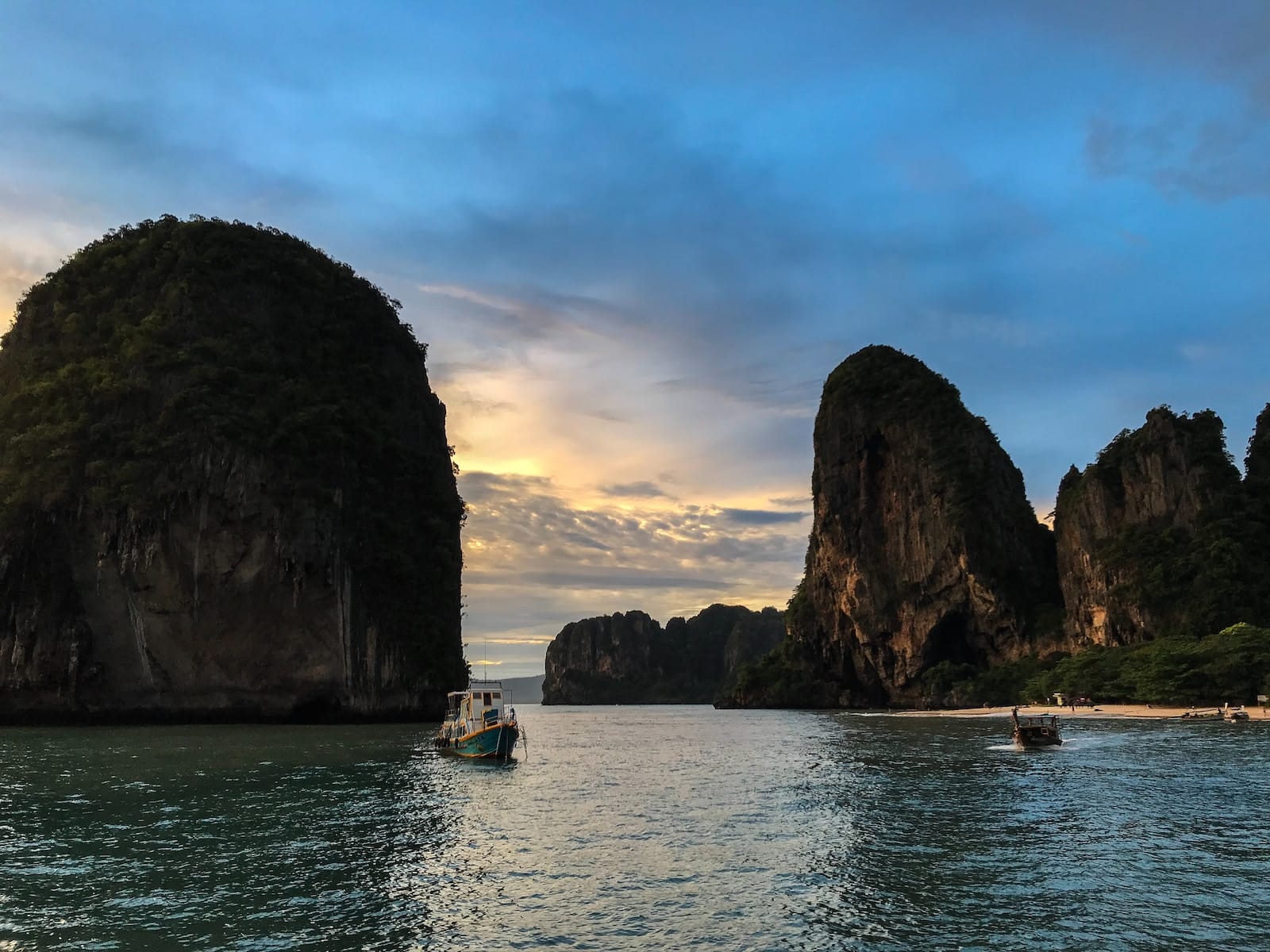 white and blue boat on sea near brown rock formation during daytime